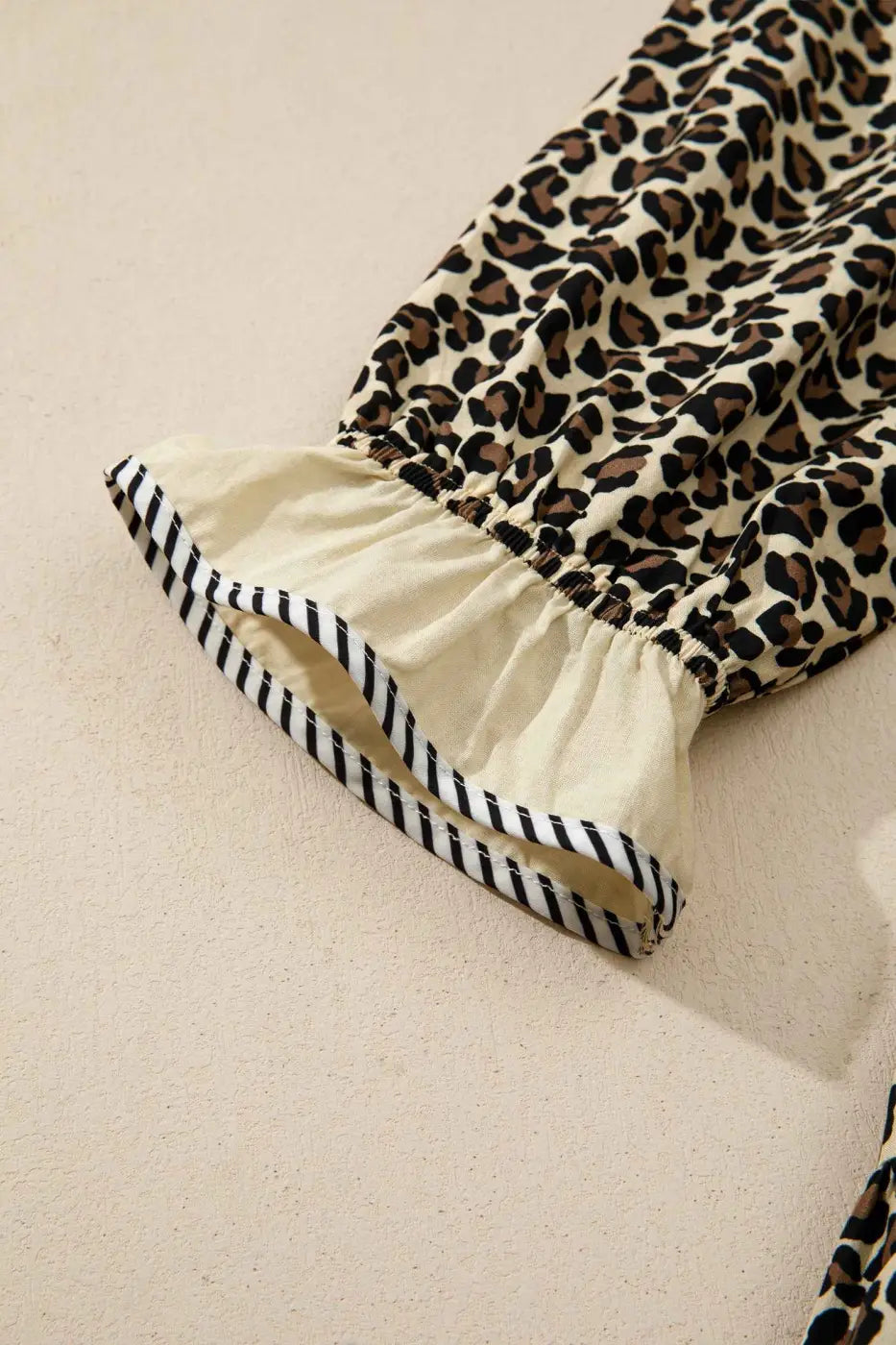 Detailed view of sleeve cuff on Leopard Print Striped Trim Mini Dress with ruffled hem and striped trim for stylish summer fashion.
