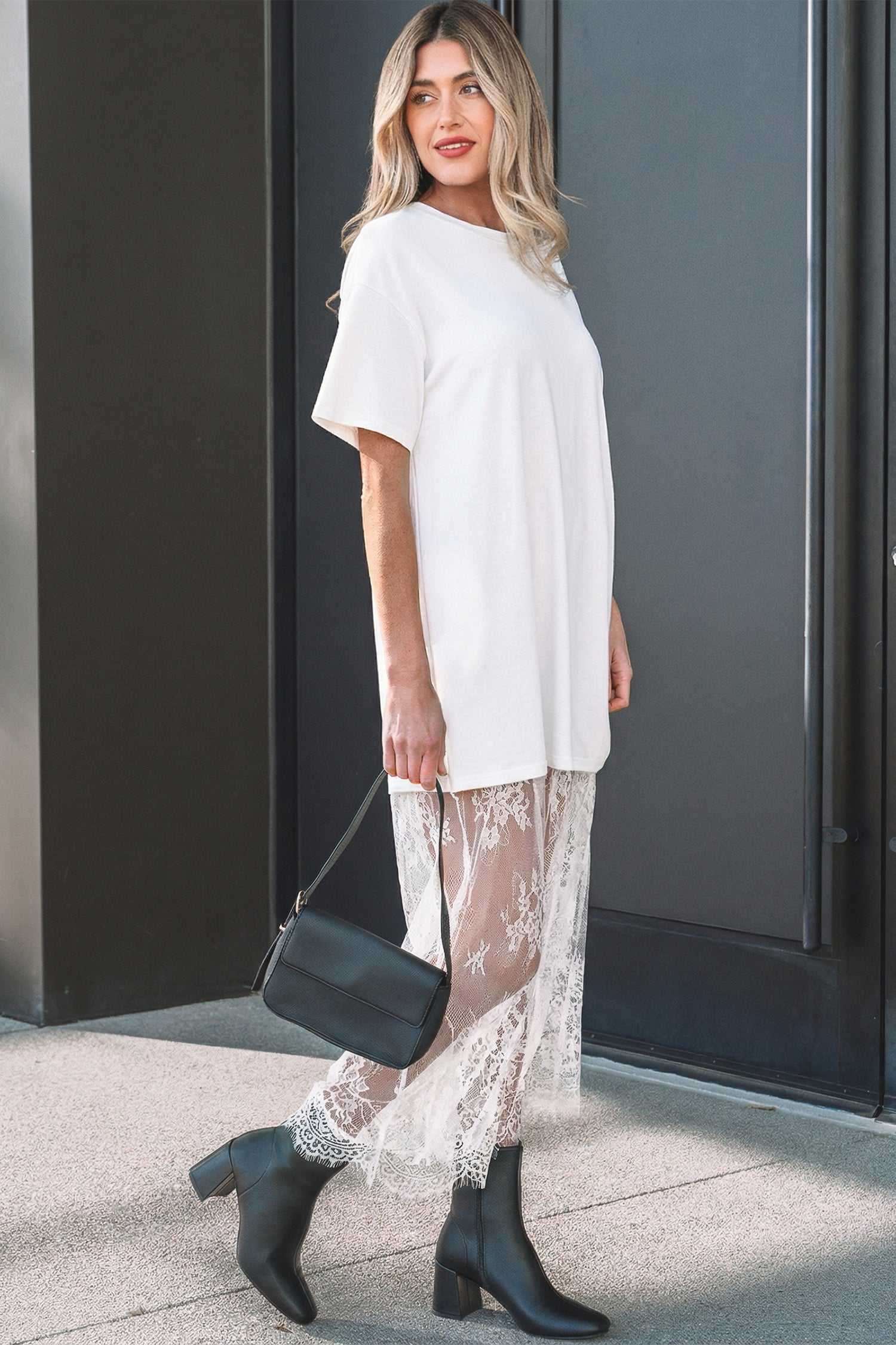 Side view of White Floral Lace Skirt Maxi Dress showcasing its H-line silhouette and floral lace skirt, paired with black accessories.