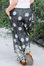 Back view of plus size black geometric print wide leg trousers with white paisley hem, styled for casual outdoor wear.