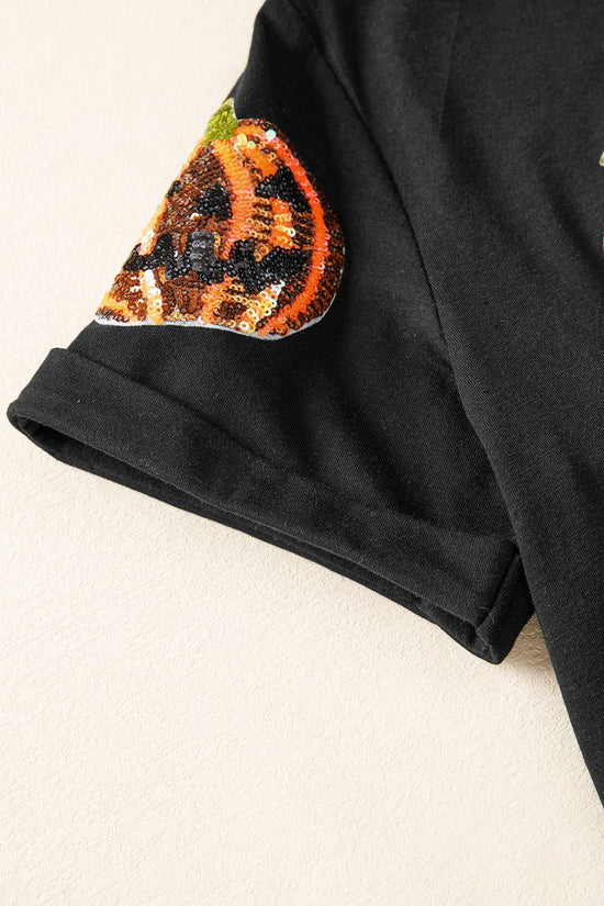 Sequin Pumpkin Face Halloween T-Shirt sleeve close-up with a decorative patch resembling a jack-o'-lantern on a beige background