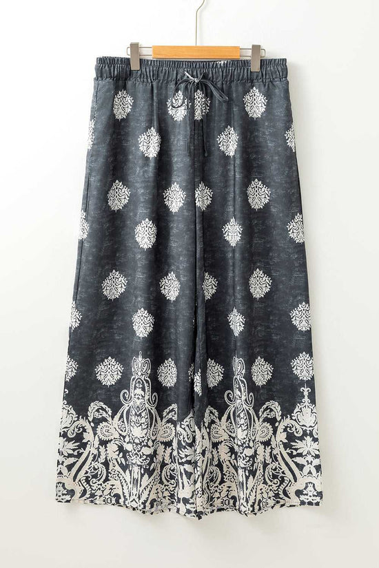 Flat lay of women's black geometric print wide leg trousers with drawstring waist and white paisley border, plus size fashion.