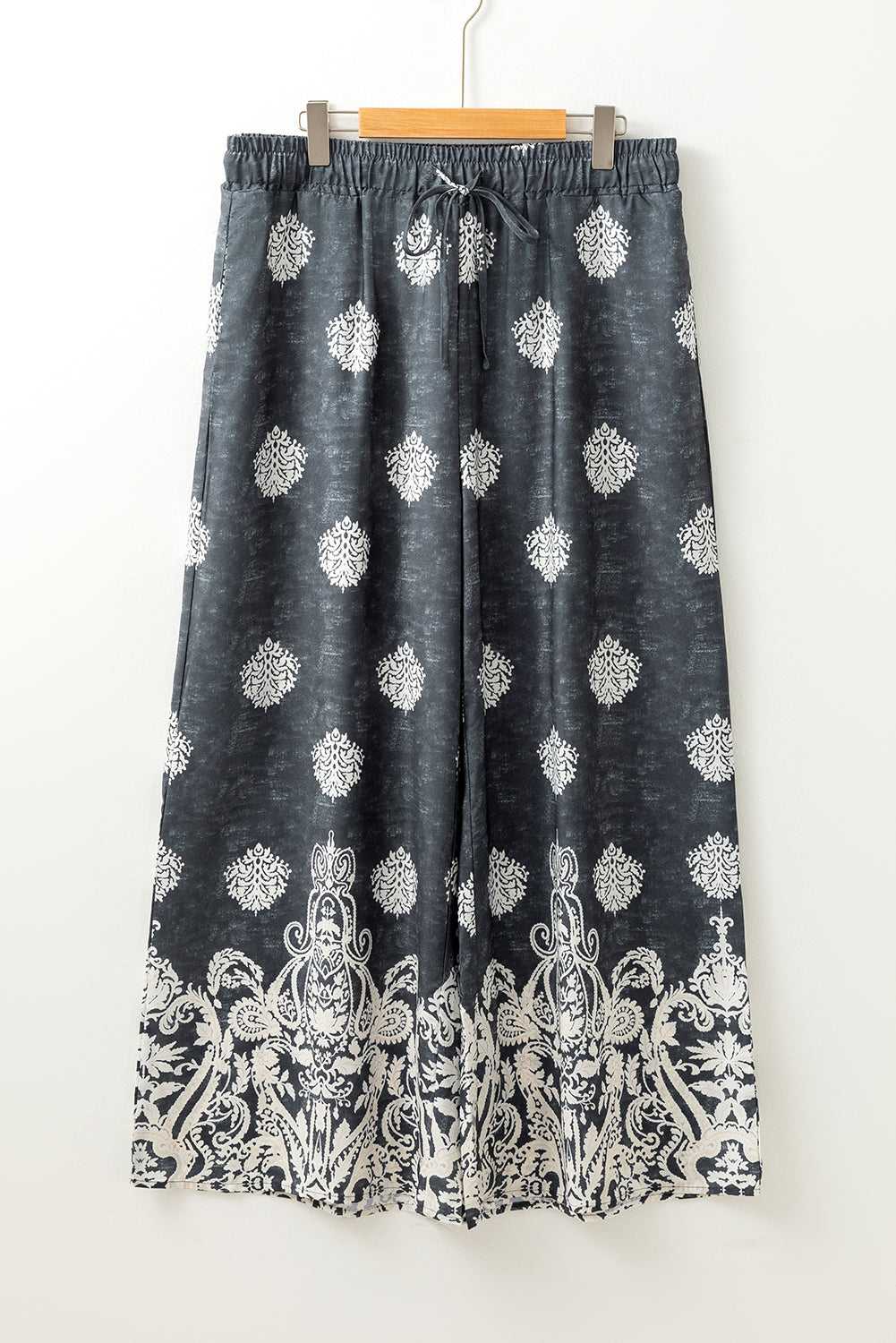 Flat lay of women's black geometric print wide leg trousers with drawstring waist and white paisley border, plus size fashion.