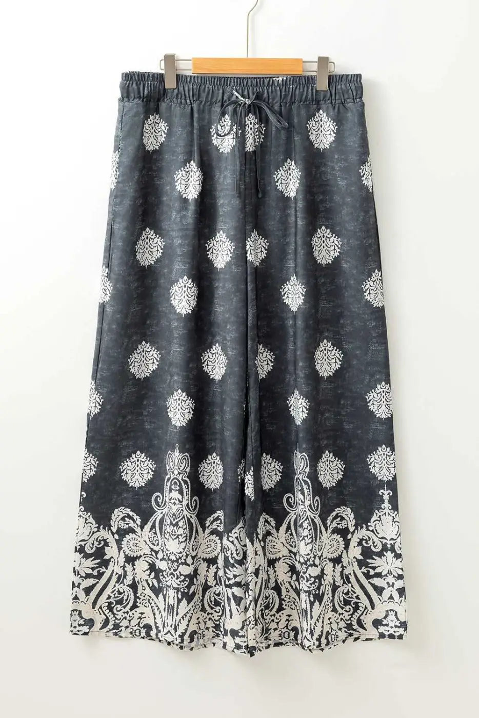 Flat lay of women's black geometric print wide leg trousers with drawstring waist and white paisley border, plus size fashion.