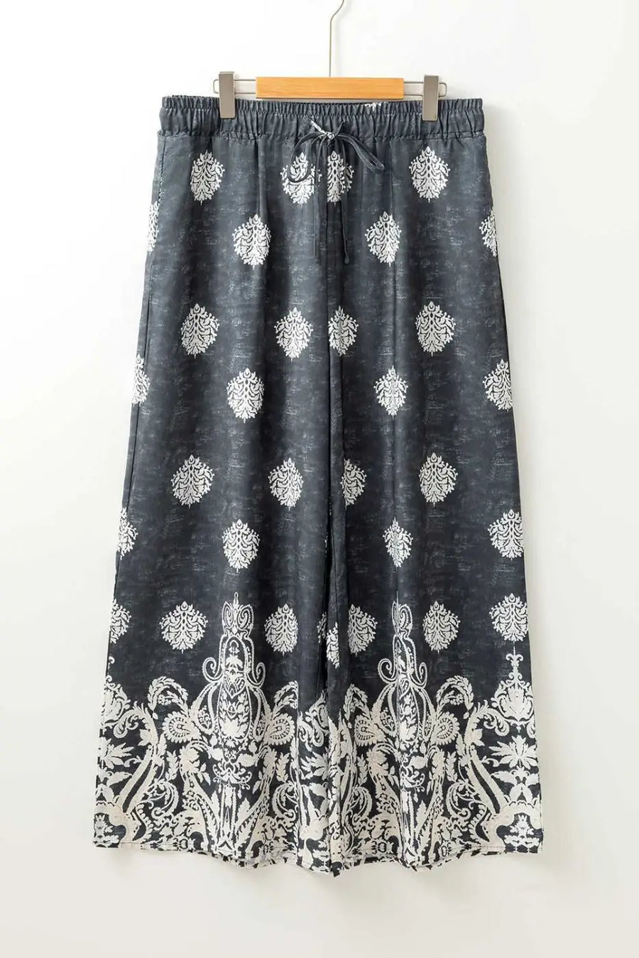 Flat lay of women's black geometric print wide leg trousers with drawstring waist and white paisley border, plus size fashion.
