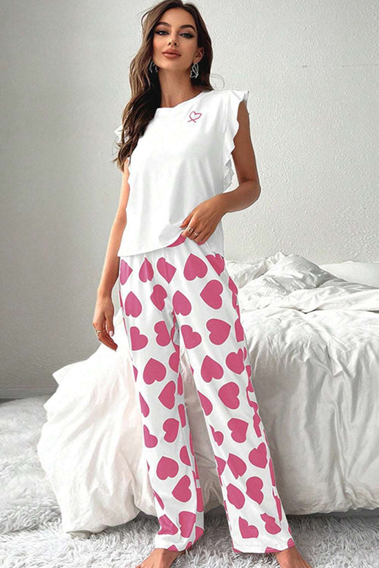 Woman wearing a white top and pink heart-patterned pants in a bedroom setting.