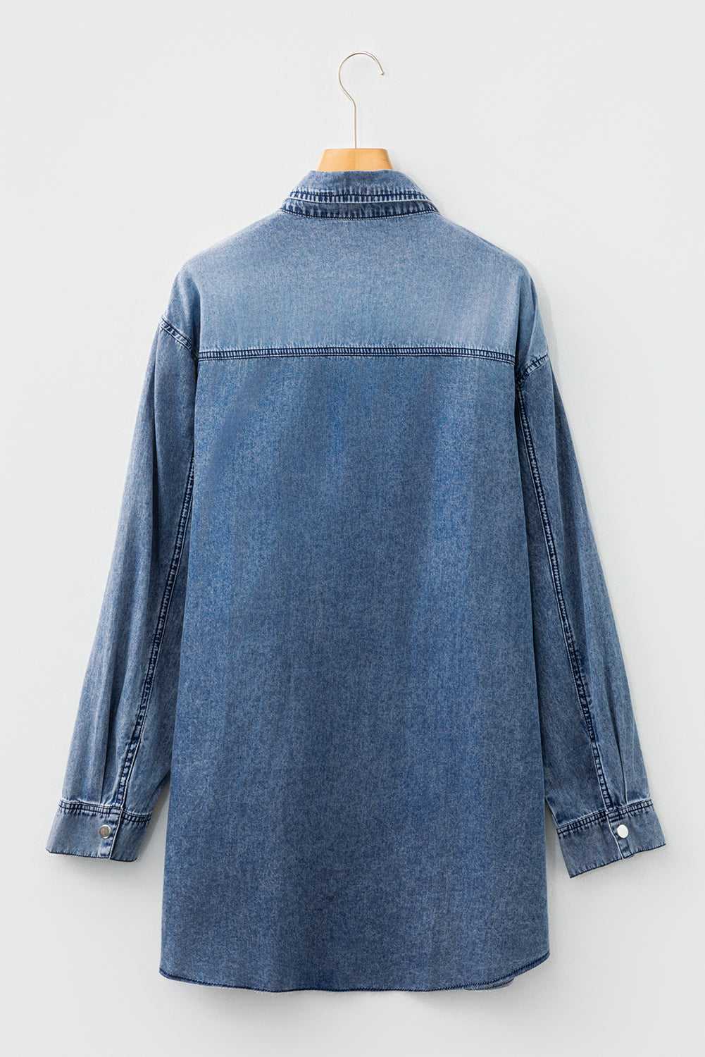 Back flat lay of oversized denim dress women in medium blue, showing long sleeves, yoke seam, and curved hem for casual autumn styling.