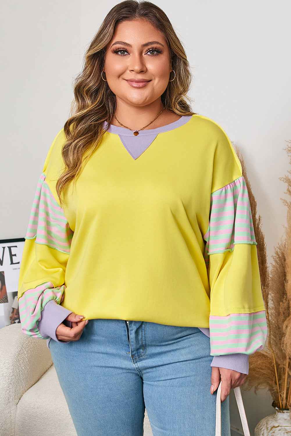 Plus size yellow sweatshirt with lilac and striped sleeves, styled casually with jeans for a cozy fall look.