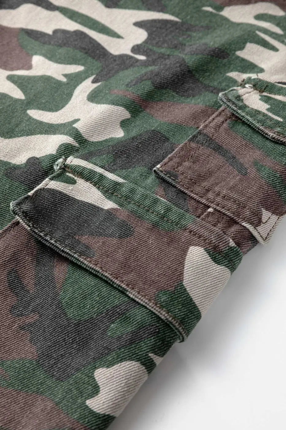 Close-up of green camo denim fabric with utility pocket detail. Durable cotton blend material used in cargo jeans for women.
