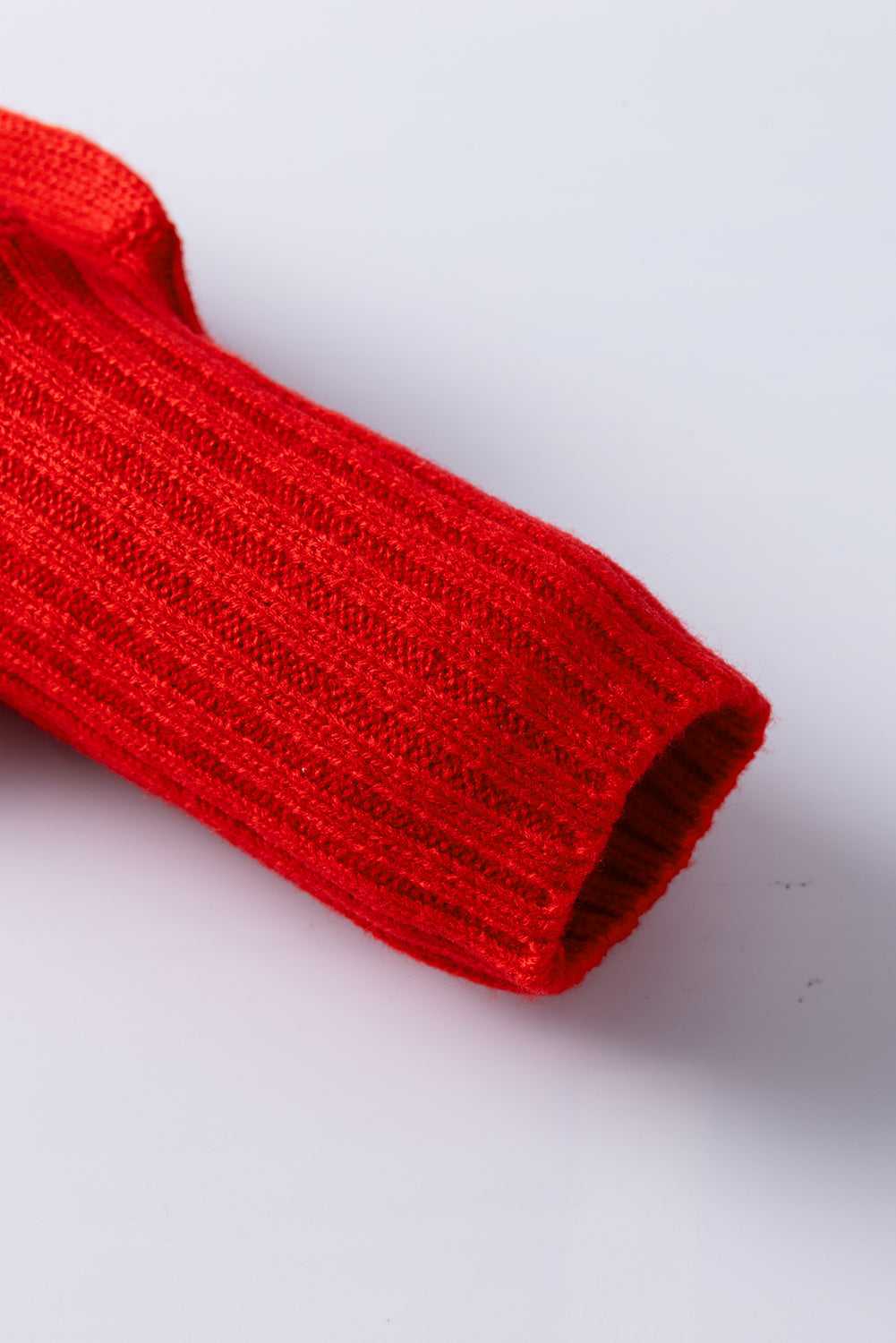 Close-up of ribbed sleeve cuff on red high neck Christmas sweater, showcasing fine acrylic knit texture for winter comfort.