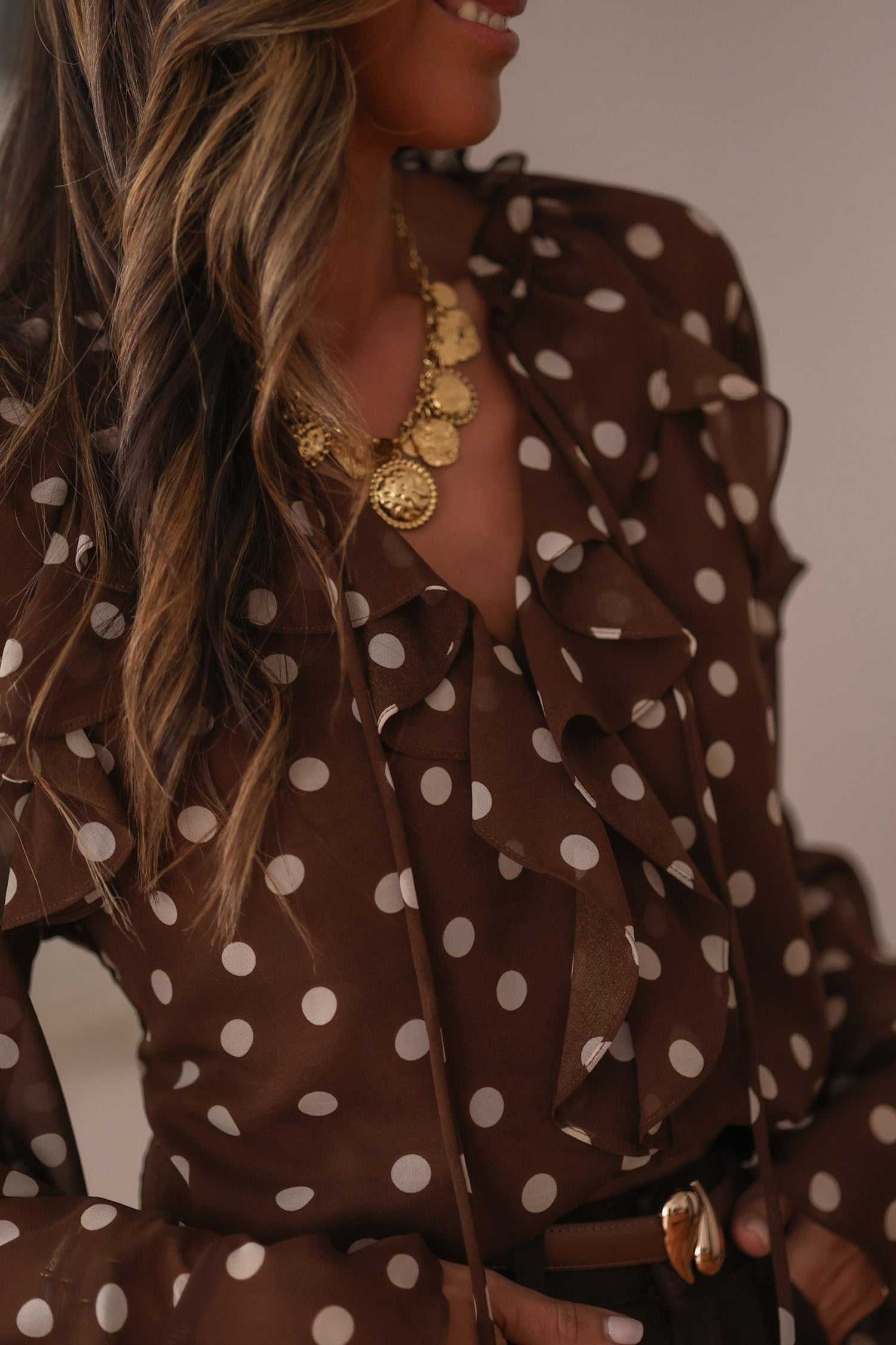 Close-up of coffee polka dot chiffon blouse showing tie neck and ruffled neckline. Feminine and elegant top for office or casual wear.