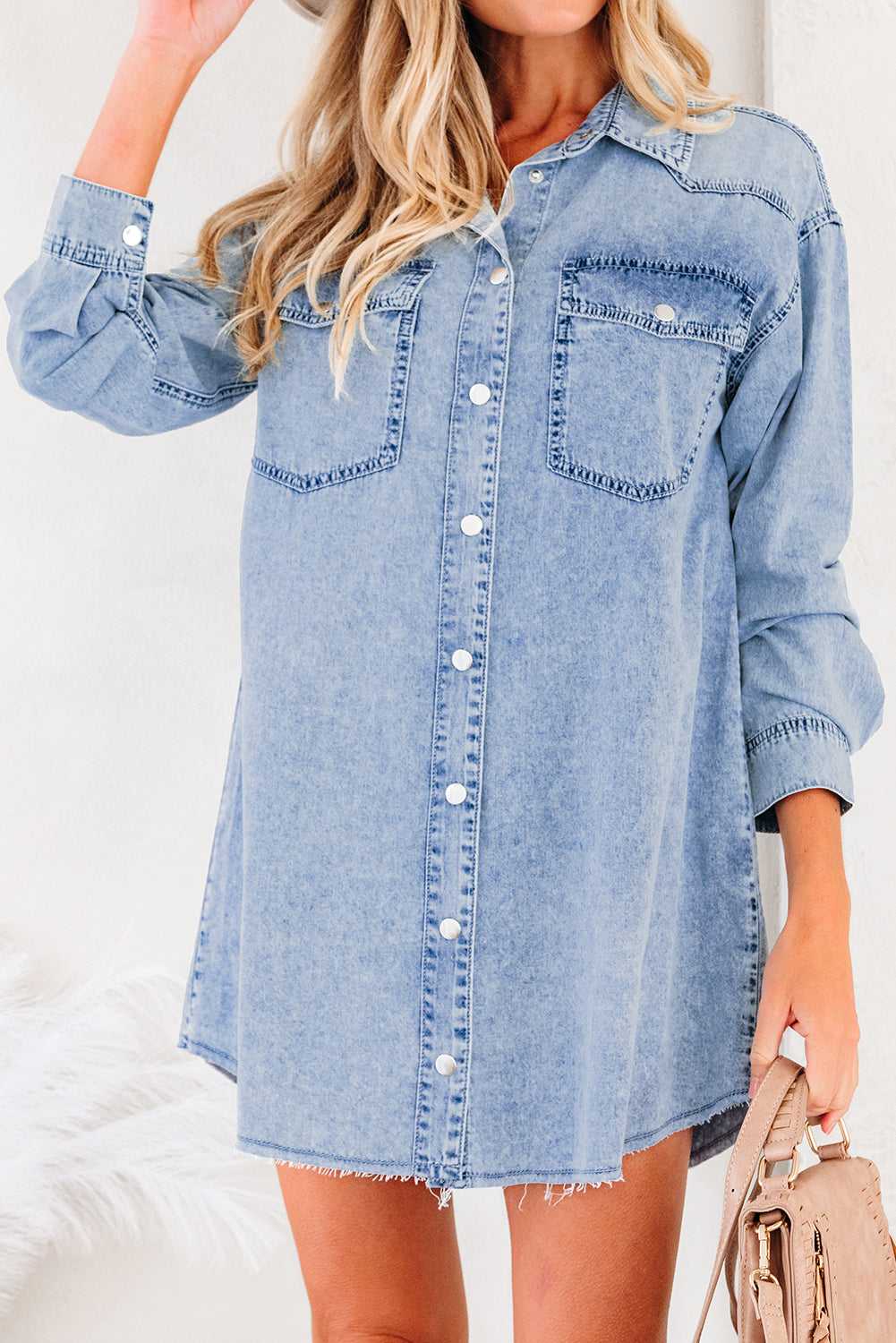 Front close-up of light blue raw hem oversized denim dress women with long sleeves, button front, and dual chest pockets for a casual look.