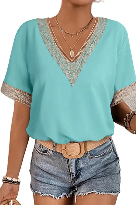 Woman wearing a light blue top with lace details and denim shorts against a neutral background