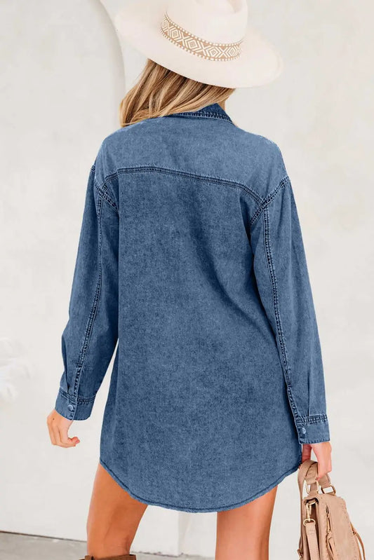 Back view of oversized denim shirt dress in medium blue with curved hem and long sleeves, showcasing relaxed silhouette and raw hem detail.