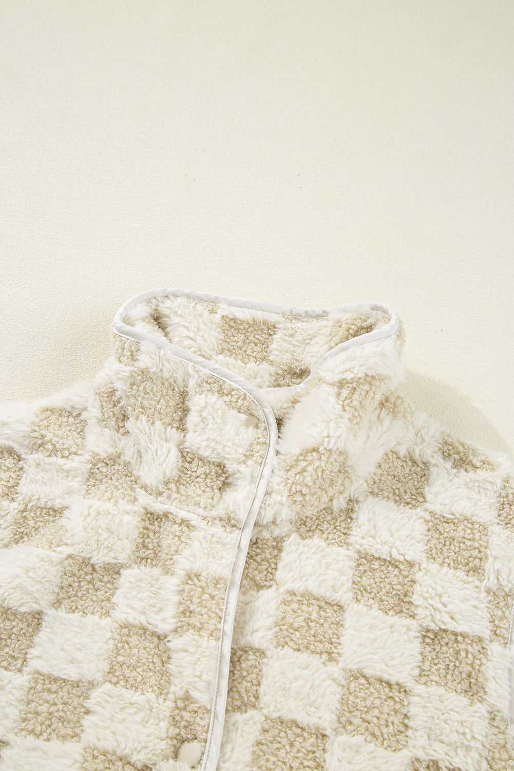 Close-up of a checkered Sherpa Fleece Vest with a neutral color scheme on a beige background