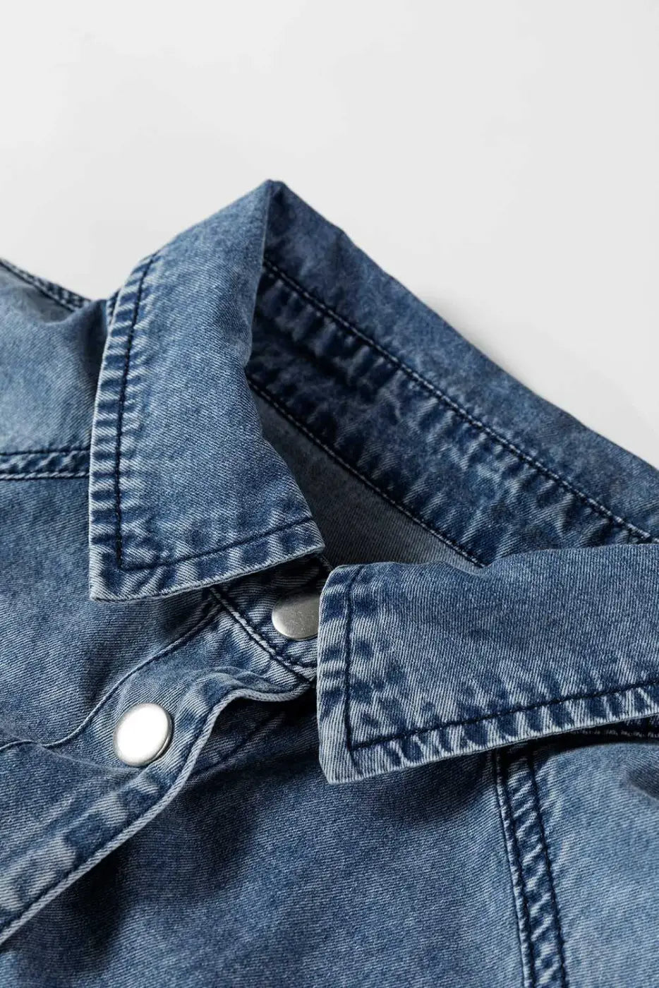 Close-up of collar and button detail on oversized denim shirt dress in medium blue, highlighting quality stitching and soft cotton denim fabric.