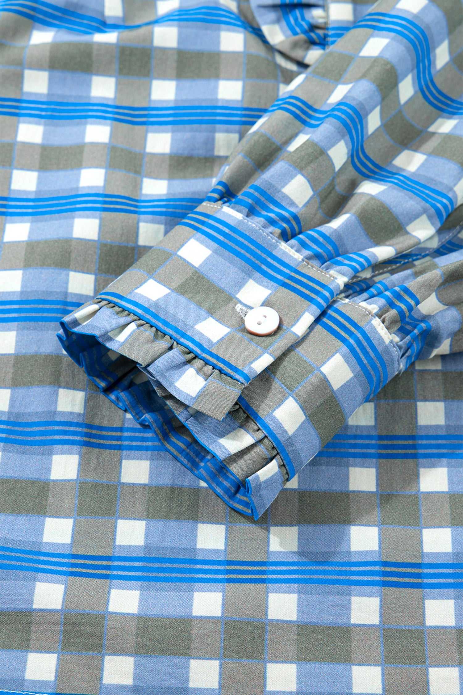 Detail of cuff on blue plaid long sleeve frilled blouse with button closure and subtle ruffle trim in soft cotton fabric.