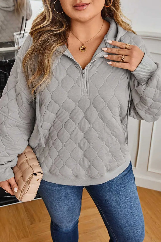 Close-up of curve grey quilted quarter-zip hoodie for women highlighting textured fabric and relaxed fit, styled with a nude clutch.