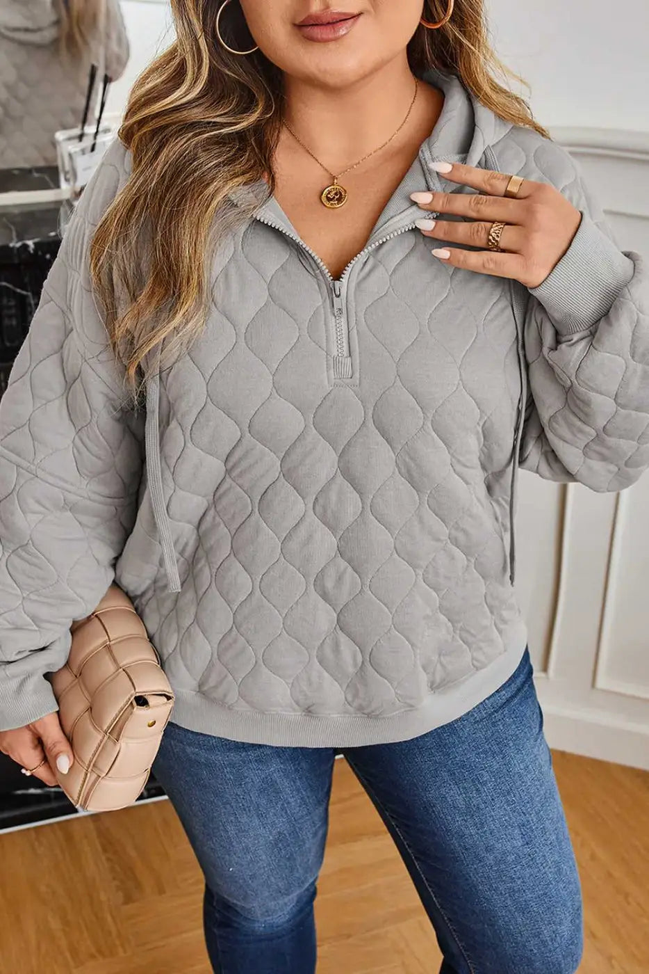 Close-up of curve grey quilted quarter-zip hoodie for women highlighting textured fabric and relaxed fit, styled with a nude clutch.