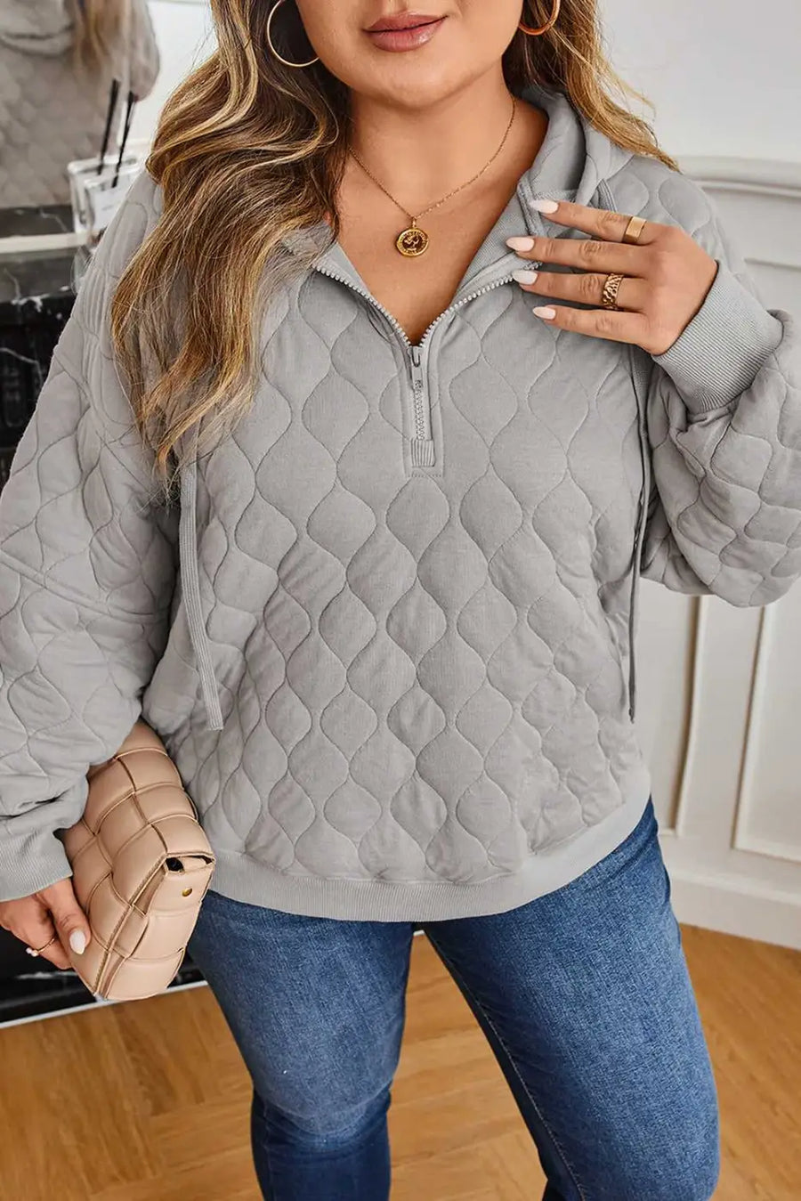 Close-up of curve grey quilted quarter-zip hoodie for women highlighting textured fabric and relaxed fit, styled with a nude clutch.