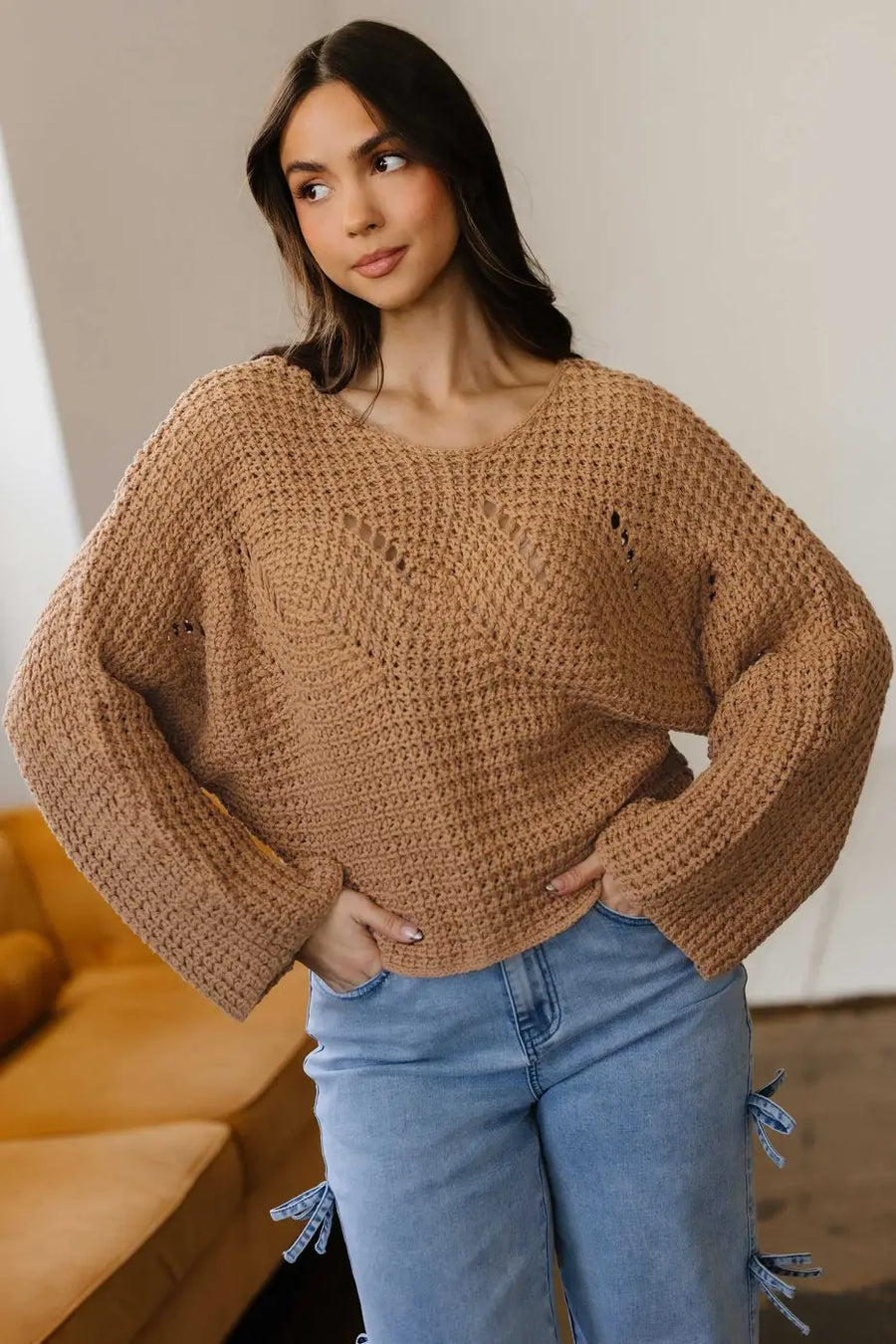 Front view of brown wide sleeve hollow knit jumper styled with light blue jeans, offering a cozy and casual fall fashion look.
