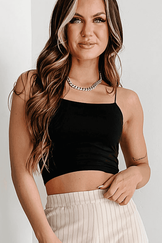 Model wearing black spaghetti strap crop top with stretch fit, styled with neutral pinstripe pants for a modern casual look.