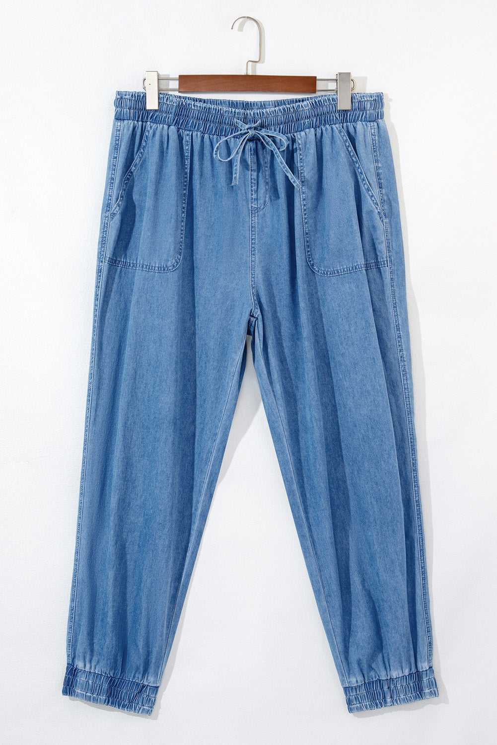 Flat lay of Plus Size Blue Denim Joggers with drawstring waist and front patch pockets, made from soft denim for everyday comfort.