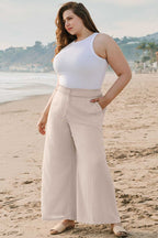 Model wearing Wide Leg Plus Linen Pants on beach, paired with white tank top. Fashionfitz casual plus size trousers for warm weather comfort.