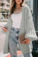 Oversized chunky knit cardigan in light grey tone, styled casually with jeans and a white top for a modern fall outfit.