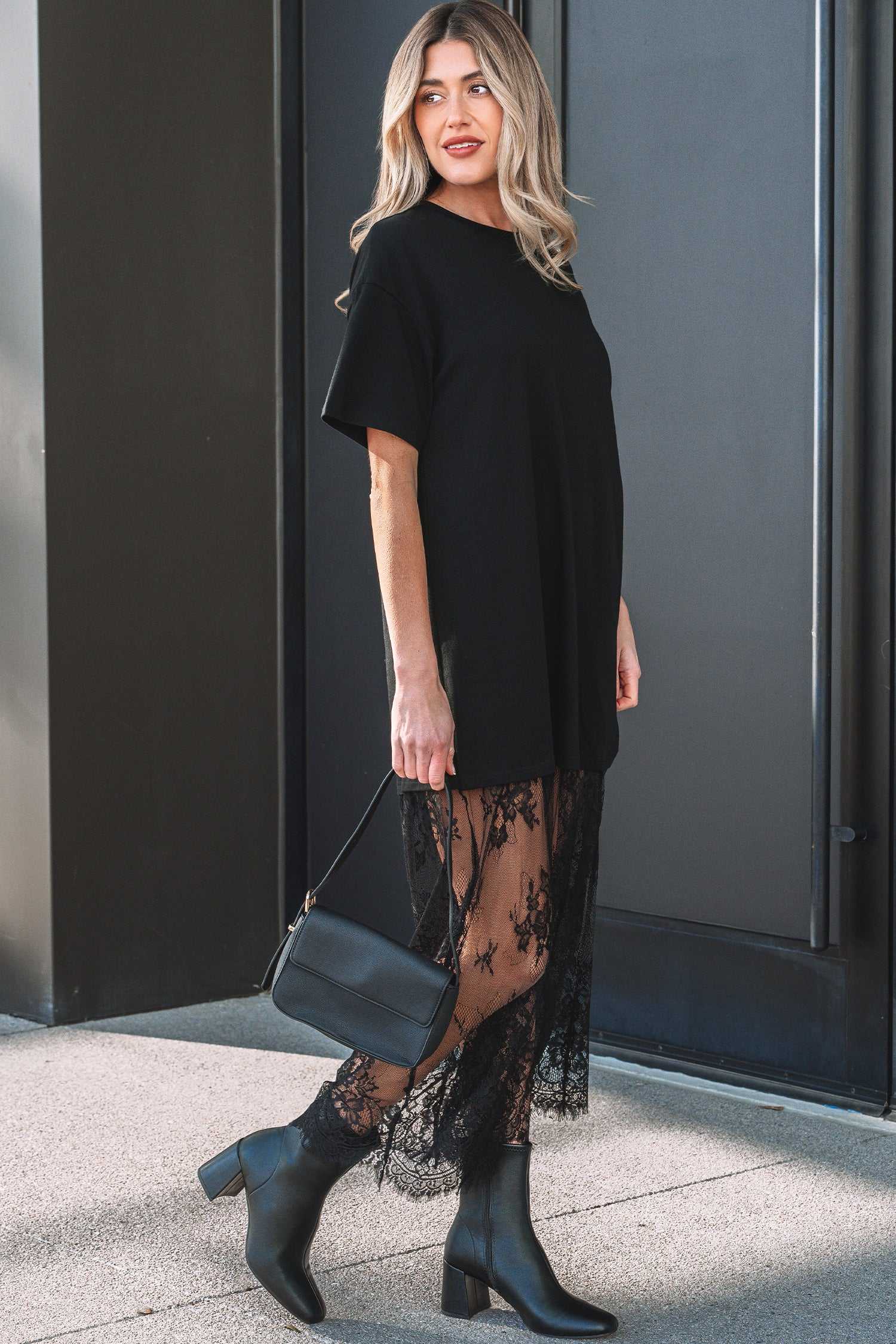 Side profile of Black Floral Lace Skirt Maxi Dress with floral lace hem and short sleeves, styled with black boots and handbag.
