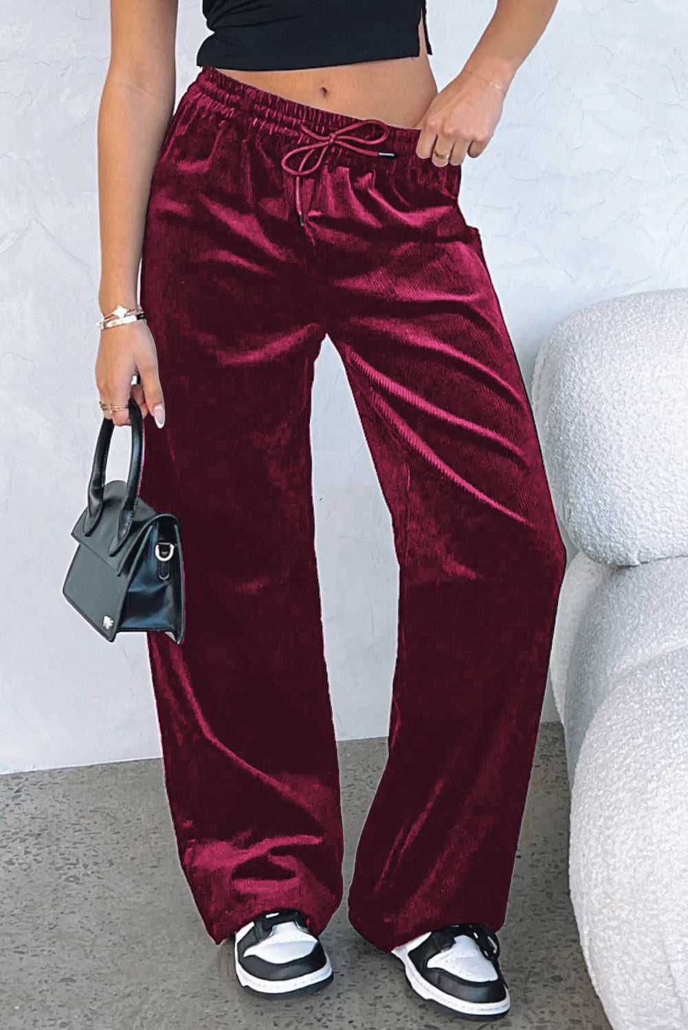 Burgundy velvet wide-leg trousers styled with a black crop top and mini handbag, ideal for casual winter outings or activewear fashion.