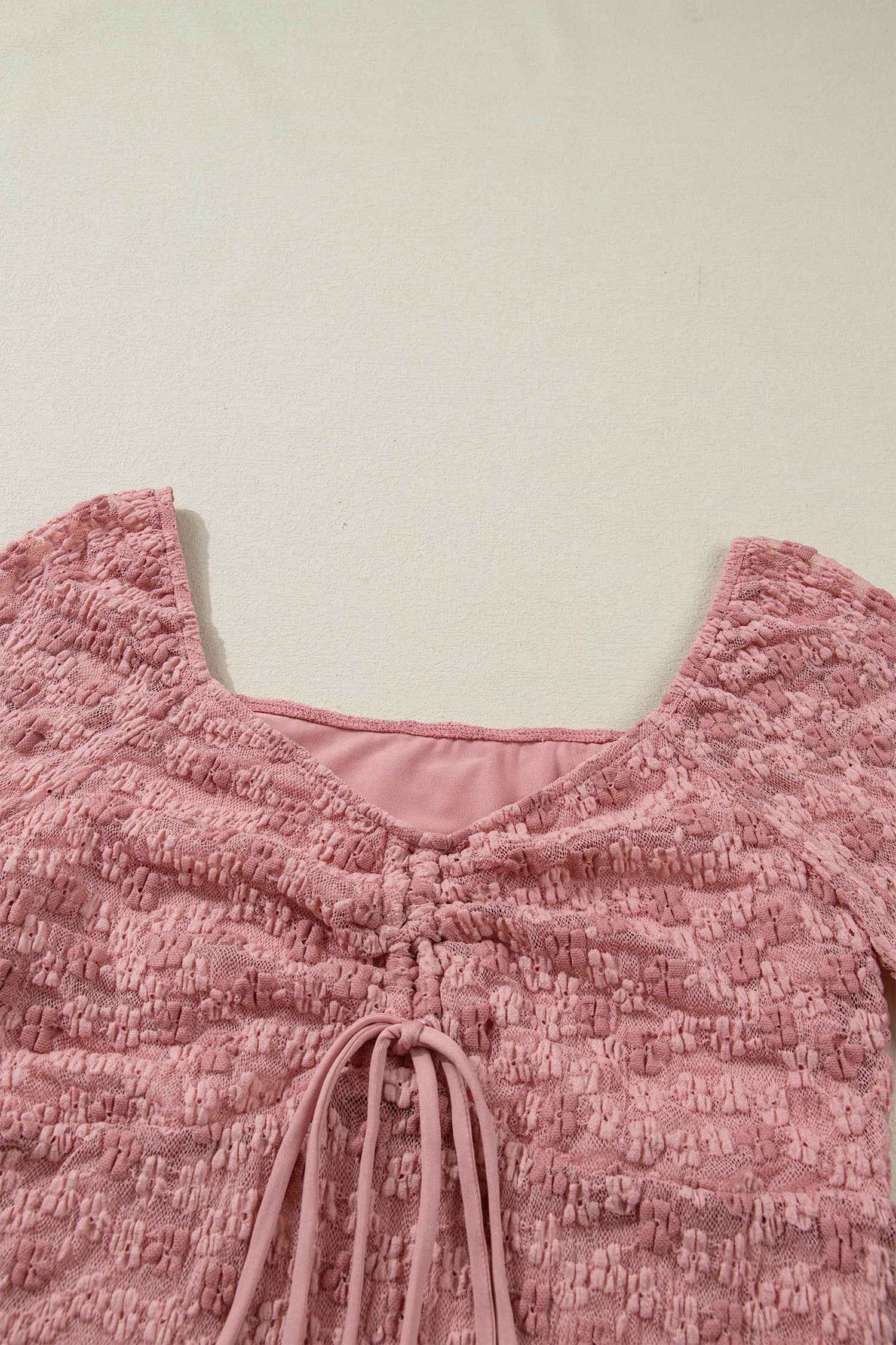 Close-up of square neckline and ruched drawstring detail on pink floral lace blouse. Soft lace texture perfect for romantic spring looks.
