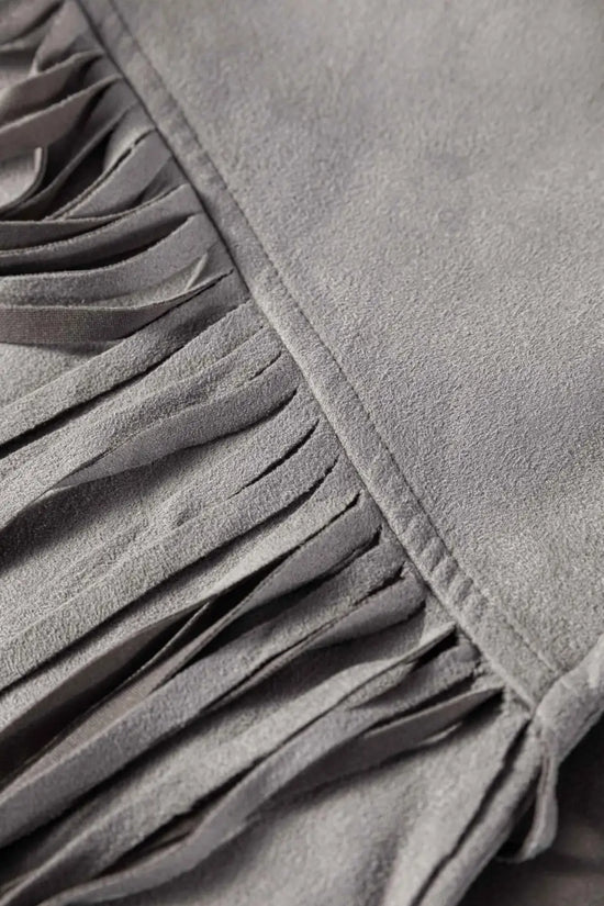 Macro shot of fringe detail on gray faux suede jacket, emphasizing movement and texture in western-inspired outerwear.