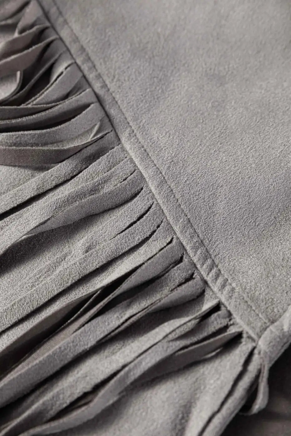 Macro shot of fringe detail on gray faux suede jacket, emphasizing movement and texture in western-inspired outerwear.