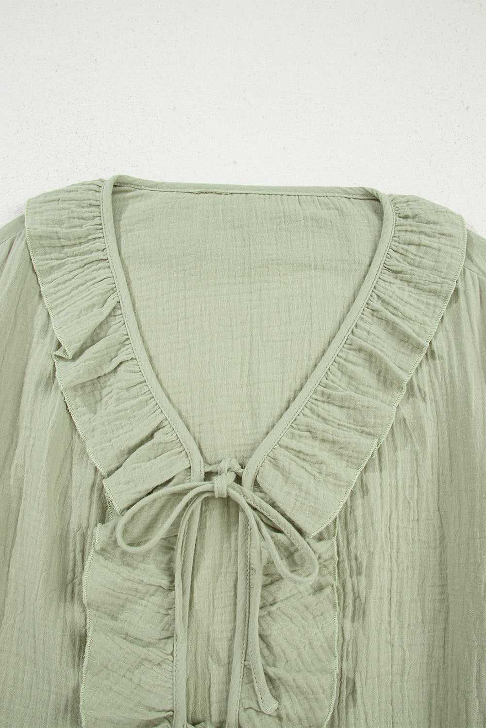 Close-up of Meadow Cotton Blouse neckline showing ruffle trim and tie detail, crafted from soft, breathable cotton fabric in solid green.