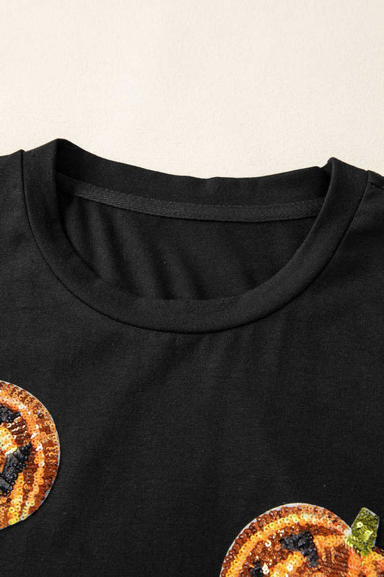 Black shirt with sequin pumpkin designs on a beige background