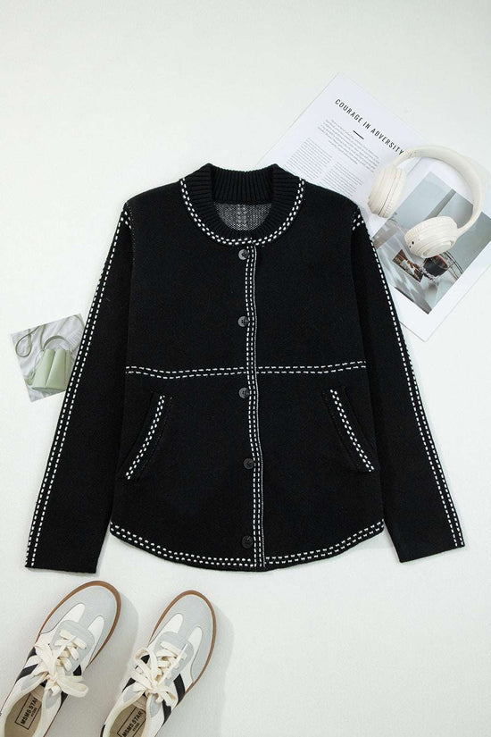Flat lay of Women's Black Contrast Trim Knitted Cardigan with front buttons and pockets, styled with sneakers and magazines.