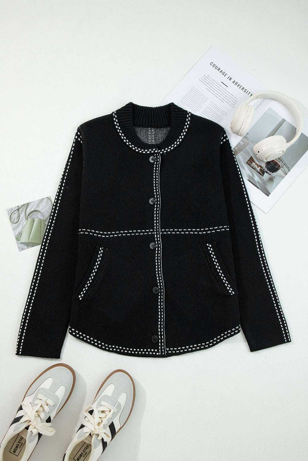 Flat lay of Women's Black Contrast Trim Knitted Cardigan with front buttons and pockets, styled with sneakers and magazines.