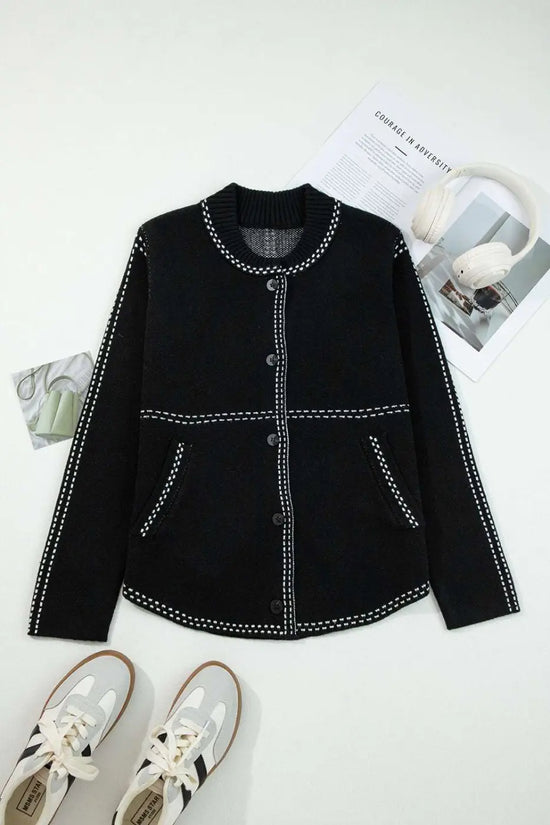 Flat lay of Women's Black Contrast Trim Knitted Cardigan with front buttons and pockets, styled with sneakers and magazines.