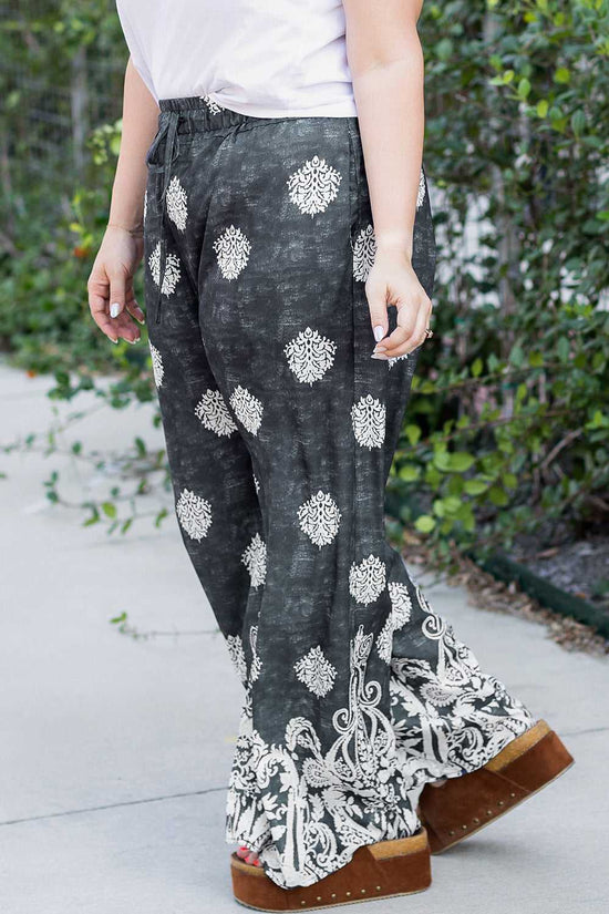 Side view of women's plus size black wide leg trousers featuring white geometric and paisley prints, paired with platform sandals.