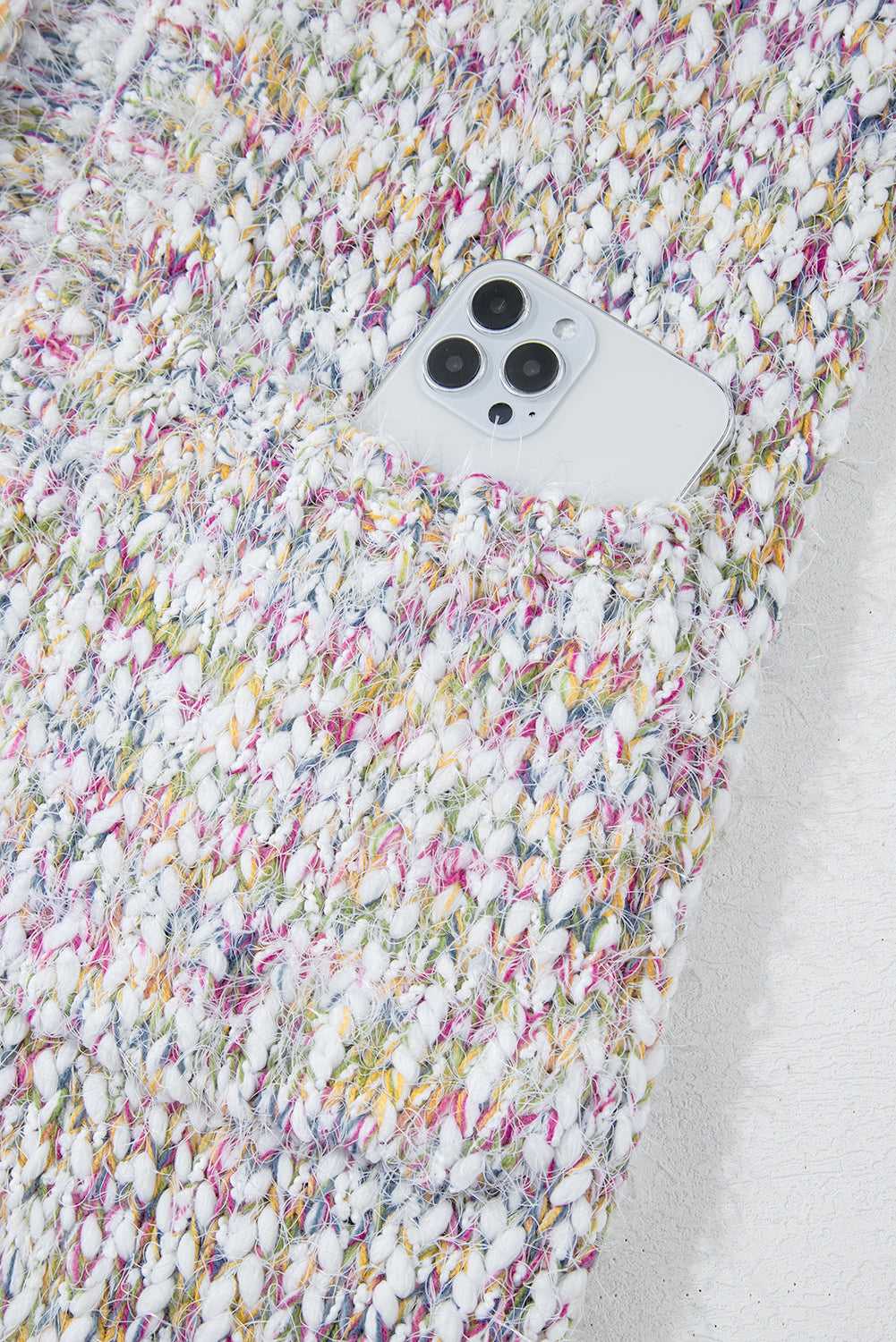 Detail of confetti knit cardigan pocket holding a smartphone, showcasing functionality and multicolor textured design.