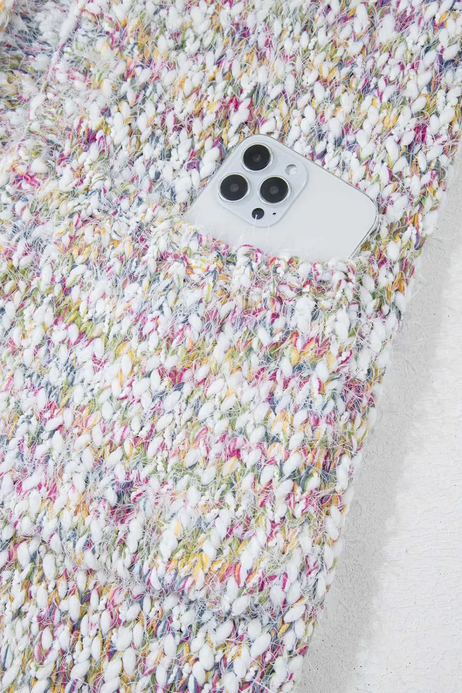 Detail of confetti knit cardigan pocket holding a smartphone, showcasing functionality and multicolor textured design.