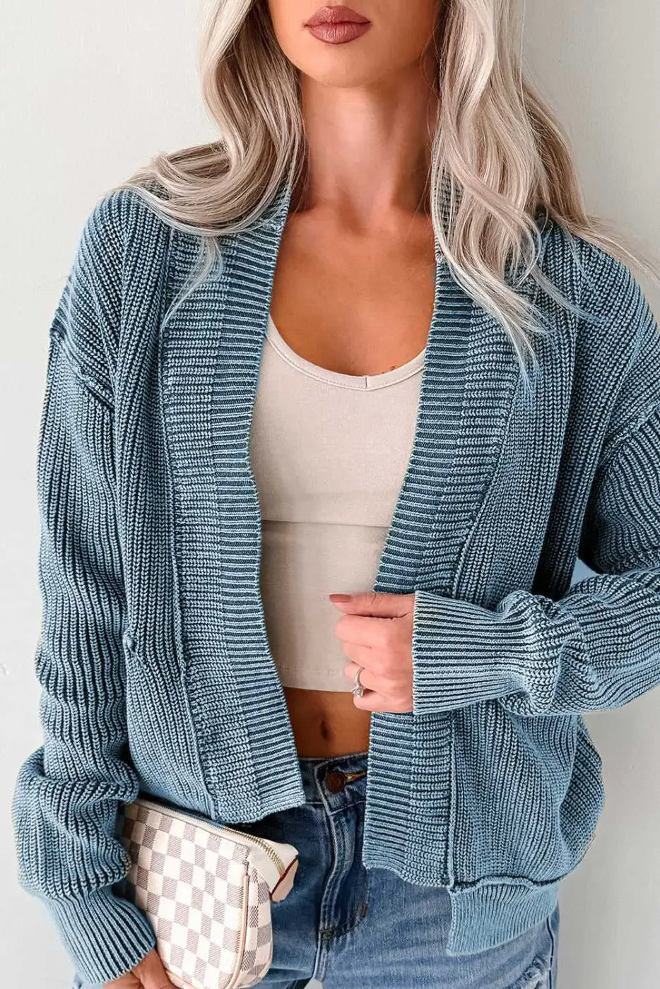 Woman in blue version of stonewash patchwork knit open cardigan, styled with crop top and jeans for a smart-casual look.