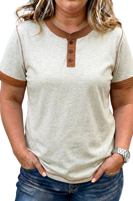 Person wearing a beige short-sleeve shirt with brown buttons and trim, paired with blue jeans.
