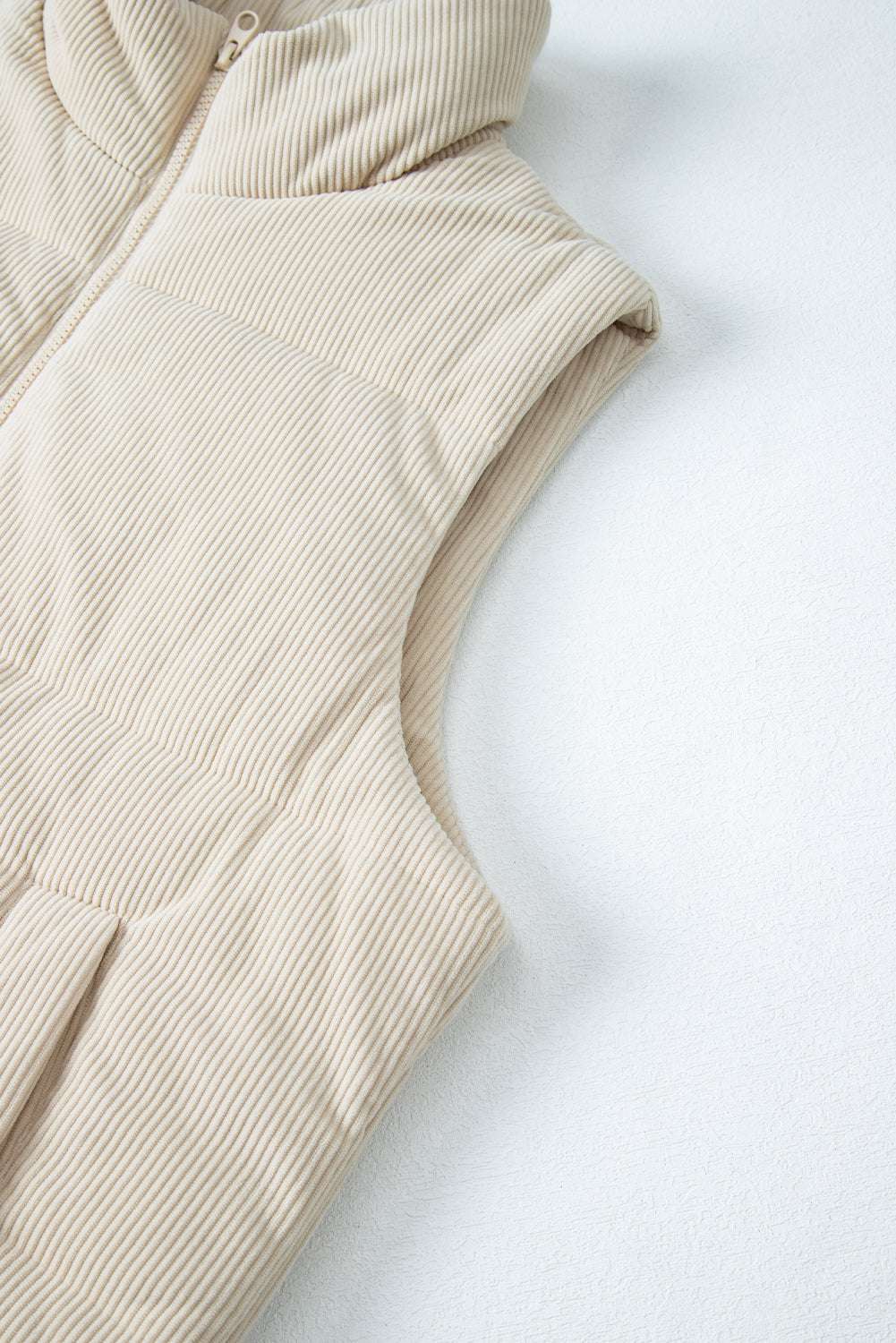 Armhole and upper section of beige corduroy puffer gilet, highlighting sleeveless cut and textured corduroy fabric.