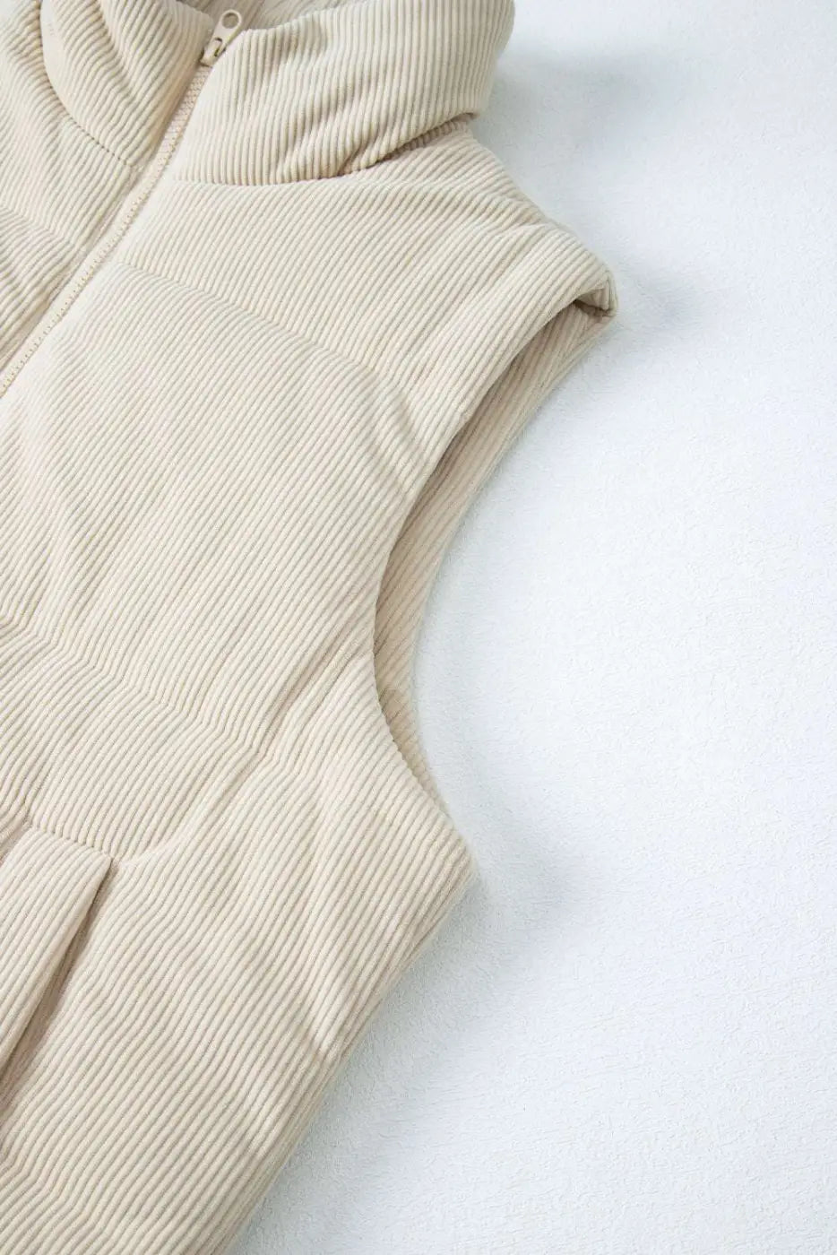 Armhole and upper section of beige corduroy puffer gilet, highlighting sleeveless cut and textured corduroy fabric.