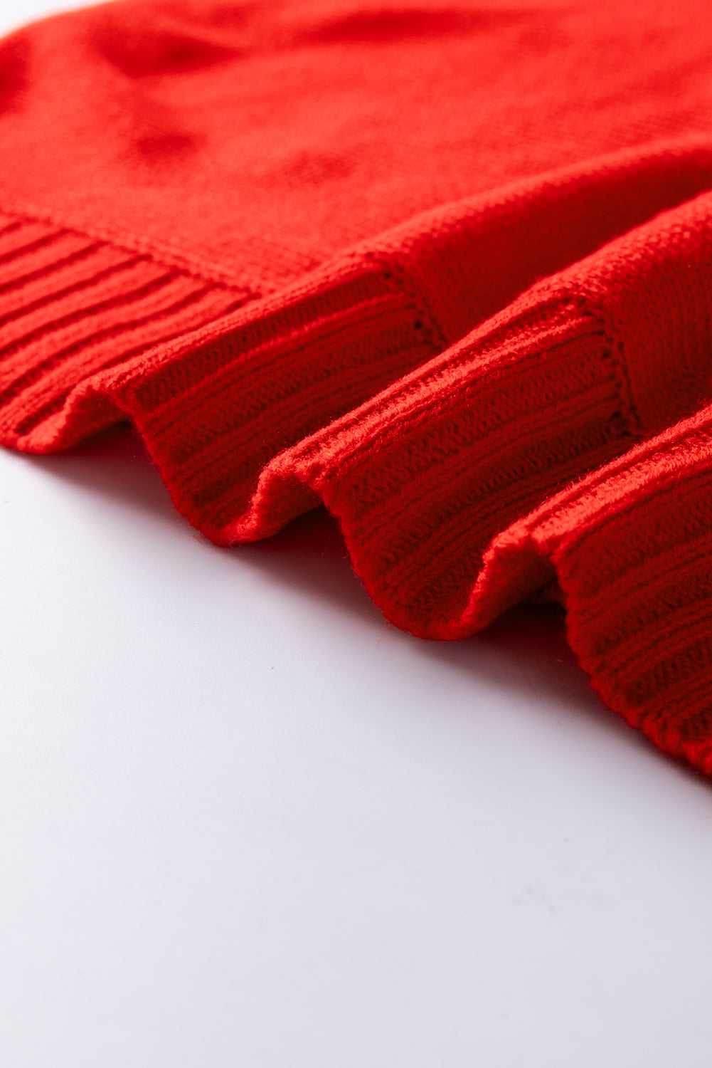 Wavy ribbed hem of red acrylic sweater, highlighting the soft texture and festive winter design.