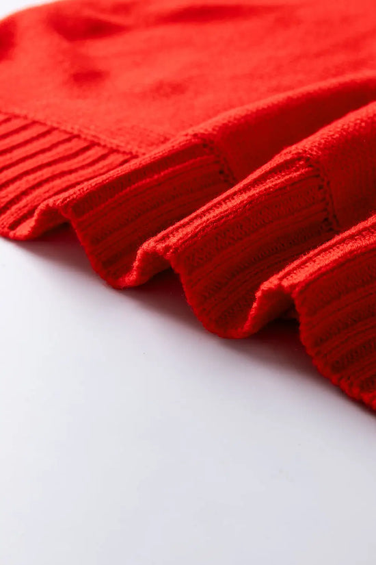 Wavy ribbed hem of red acrylic sweater, highlighting the soft texture and festive winter design.