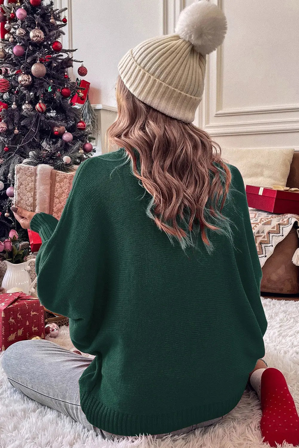 Back view of green Stylish High Neck Red Sweater - Christmas, styled with a beanie and surrounded by holiday gifts under a Christmas tree.