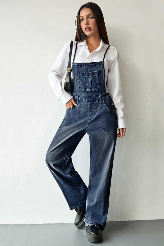 Women's casual dark blue baggy denim overalls with front bib pocket and wide legs. Styled with a white blouse and black handbag.