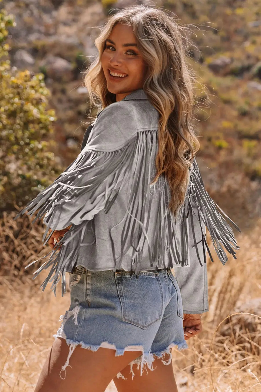Side view of gray cropped fringe faux suede jacket styled in outdoor setting, ideal for casual western fall fashion.